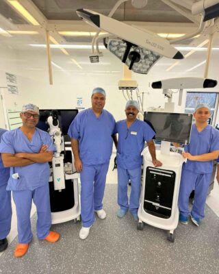 A group of four medical professionals in scrubs stand in a modern hospital operating theatre, smiling amid advanced equipment. Text reads: back to your active lifestyle again with VELYS robotic-assisted knee surgery from Joint Reaction 01252 851285