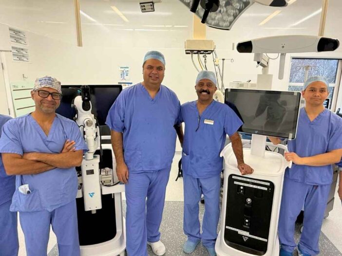 A group of four medical professionals in scrubs stand in a modern hospital operating theatre, smiling amid advanced equipment. Text reads: back to your active lifestyle again with VELYS robotic-assisted knee surgery from Joint Reaction 01252 851285