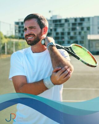 Man in tennis kit on a court, grimacing in pain and holding his elbow while clutching a racquet. Text overlay discusses tennis elbow, highlighting the importance of seeking expert care from Joint Reaction orthopaedic surgeons.