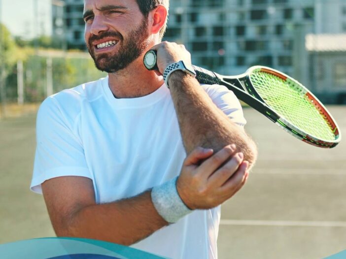 Man in tennis kit on a court, grimacing in pain and holding his elbow while clutching a racquet. Text overlay discusses tennis elbow, highlighting the importance of seeking expert care from Joint Reaction orthopaedic surgeons.